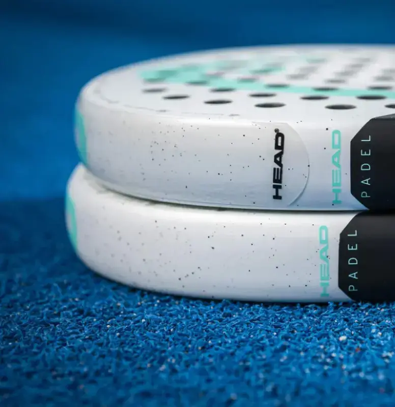 Head Antishock Skin Paddle Anwendung Nahaufnahme zwei tuerkise Padelschlaeger auf blauem Court mit aufgeklebtem Rahmenschutzstreifen am Rahmen