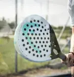 Head Antishock Skin Paddle Lifestyle Hand haelt tuerkisen Padelschlaeger auf Court mit aufgeklebtem Rahmenschutzstreifen am Rahmen