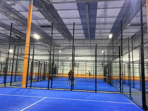 Indoor-Padelhalle mit mehreren MS Manza Plätzen, blauer Kunstrasen mit orangen Banden