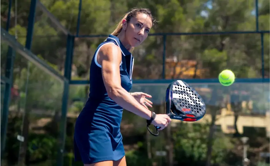 Spielerin mit Padel Schläger beim Padel allein trainieren im Volley mit konzentriertem Blick auf den Ball