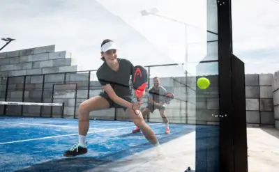 Padelball springt an der Glaswand ab, während ein Spieler ihn erwartet